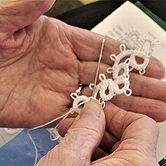Closeup of an elderly woman's hands, displaying a bit of lace she is making, with needle and thread attached